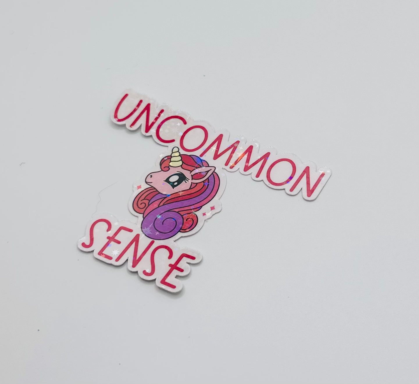 holographic sticker with stars. Pink and purple unicorn on a light pink background with the words "uncommon sense" in pink writing