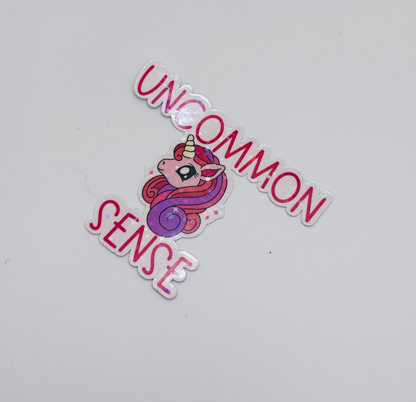 holographic sticker with stars. Pink and purple unicorn on a light pink background with the words "uncommon sense" in pink writing