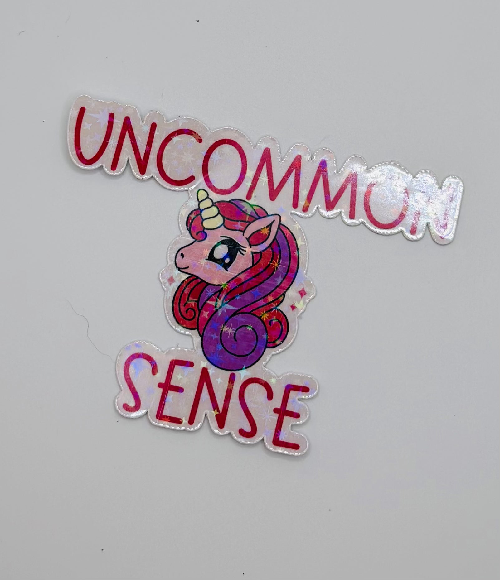 holographic sticker with stars. Pink and purple unicorn on a light pink background with the words "uncommon sense" in pink writing