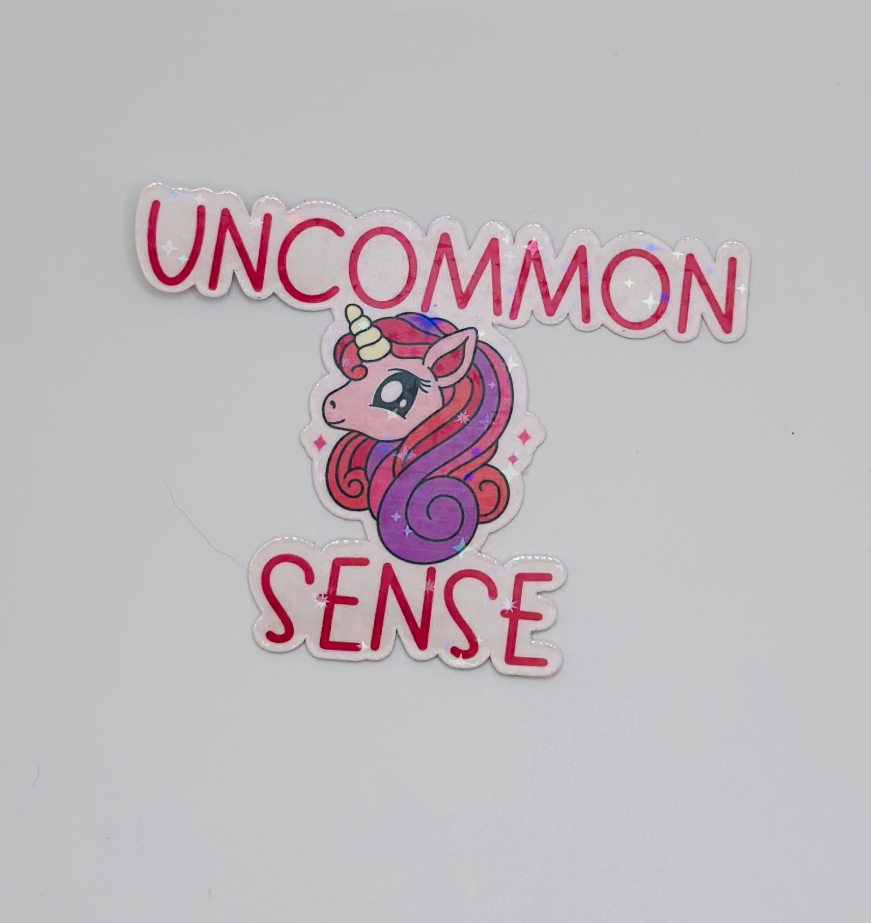 holographic sticker with stars. Pink and purple unicorn on a light pink background with the words "uncommon sense" in pink writing